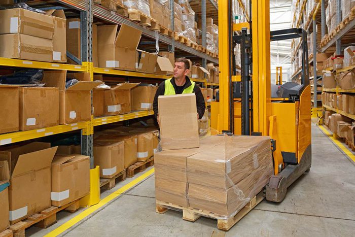 Man in Public Warehouse Stacking Boxes on Packed Shelves