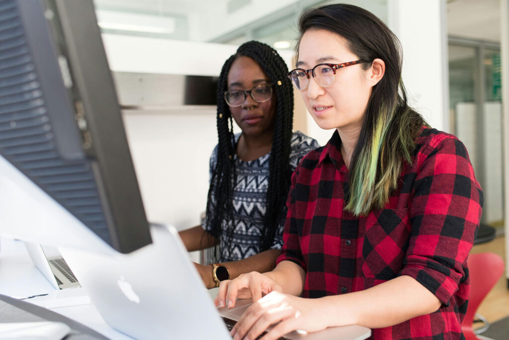 Two women analyzing warehouse management system software on computer screen for e-commerce order fulfillment optimization.